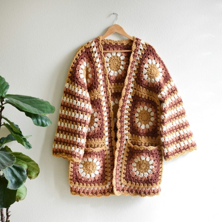 A finished crocheted cardigan hanging on a wall beside a potted plant