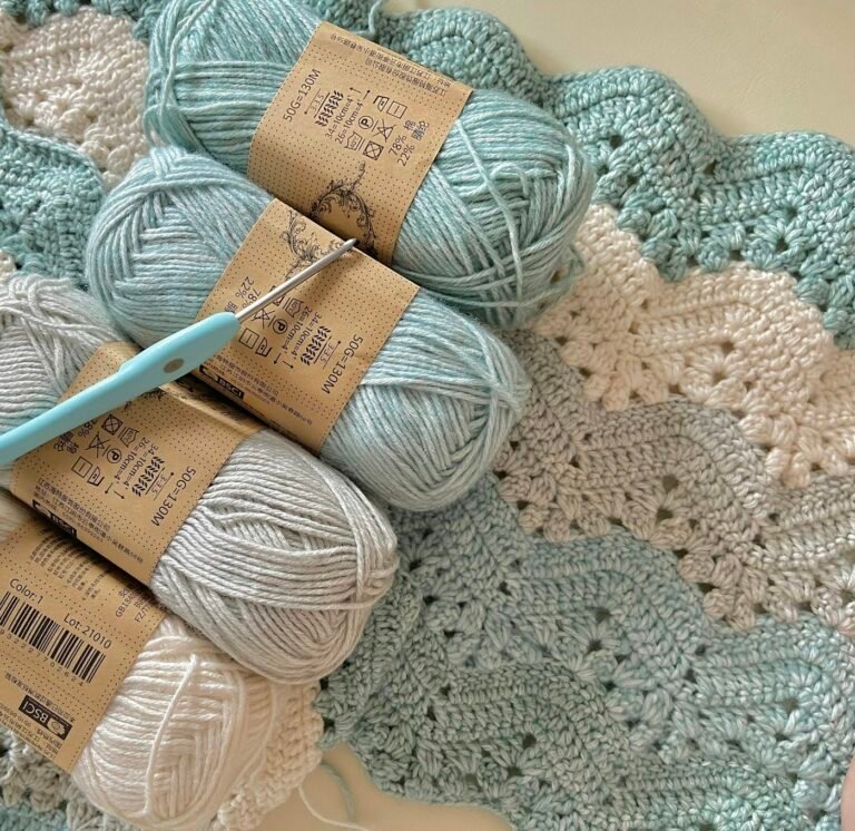 Three balls of yarn and a crochet hook resting on a blanket
