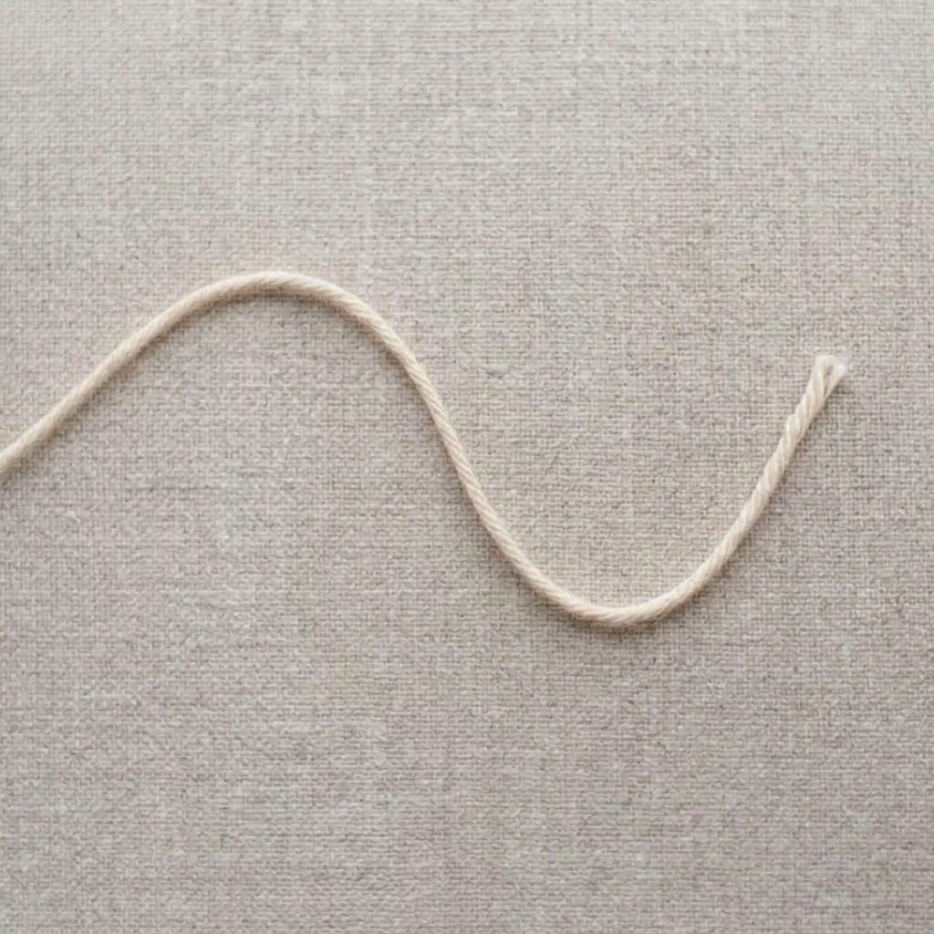 One strand of cream yarn laid out with a short tail at one end and the working yarn at the other